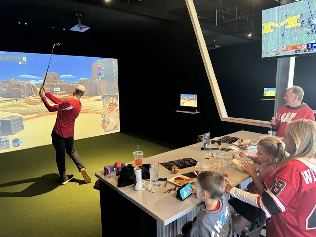 Family enjoying a golf simulator bay with dining setup at The Bogey Factory